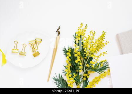 Beautiful spring composition featuring yellow mimosa flowers oblique calligraphy pen clips and blank paper on white wooden surface ideal for greeting Stock Photo
