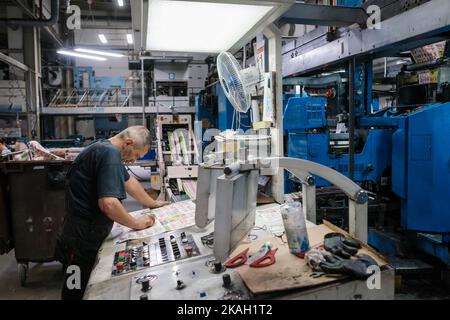 Vilnius, Lithuania - October 12, 2022: Side view of serious middle aged man with newspaper sample pressing buttons on control panel of machine during Stock Photo