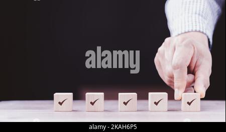 Checklist Survey and assessment concept, human hand putting cube wood with Check mark icon on wooden blocks, gray background with copy space Stock Photo