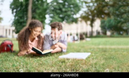 blurry image of students reading a textbook lying on the grass. Stock Photo