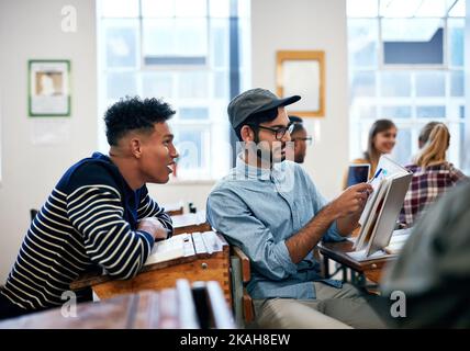 Helping each other will help understand things better. university students going through notes together in class. Stock Photo