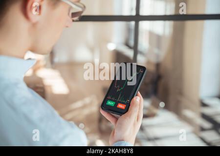 Close up view image of man checking bitcoin price chart on digital stock market app on smartphone, trying to predict future price action of cryptocurrency Stock Photo