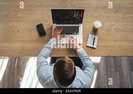 Top view of businessman trading cryptocurrency looking at laptop with stock market app, sitting at table desk, making analysis of digital money charts, investor broker analyzing indexes. Copy space Stock Photo