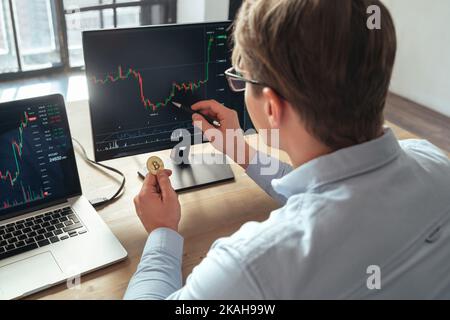 Business man trader investor holding golden bitcoin buying or selling cryptocurrency tokens, analyzing chart of stock market and investment risks online on pc Stock Photo