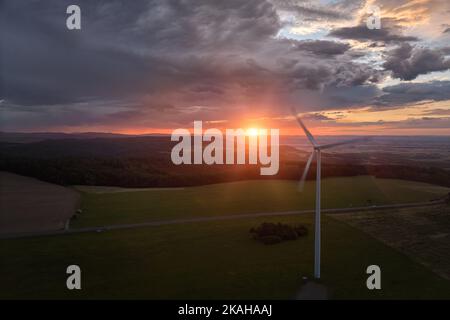 Aerial view of wind  power plant in full load, illuminated with dramatic light, green landscape against sunset sky with clouds. Aerial, drone inspecti Stock Photo