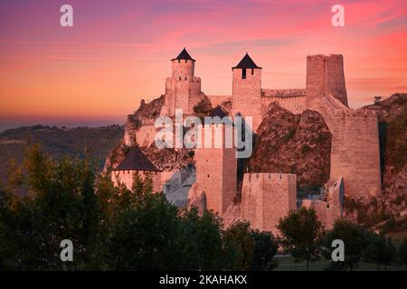 The medieval fortress of Golubac illuminated of pink light of setting sun against colorful clouds in background. Famous tourist place, Serbia. Stock Photo
