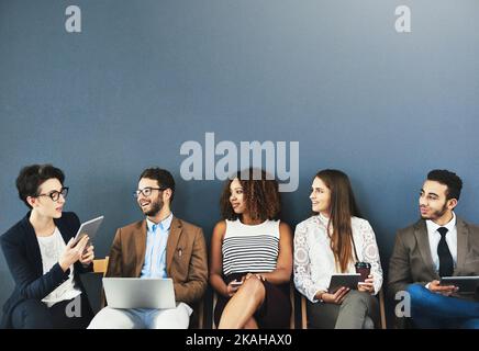 Connecting with the other candidates. Studio shot of a group of businesspeople using wireless technology and talking while waiting in line against a Stock Photo