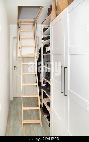 Wooden ceiling pull down attic folding stairs in small minimalist hallway corridor, space saving in home concept. Stock Photo
