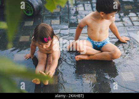 Two happy little kids having fun to play with the rain together in the backyard. Rainy day. Happiness concept. Summer outdoor fun activity. Stock Photo