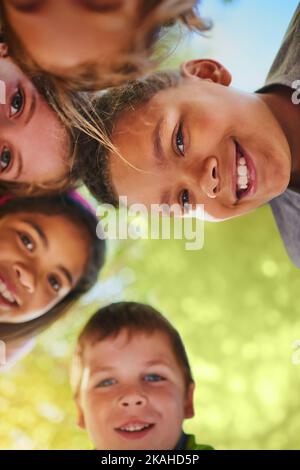 Putting our heads together to decide what to play next. a diverse group of young friends huddled together outside. Stock Photo