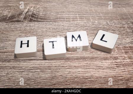 Lettered plastic tiles on wooden board displaying the acronym HTML (HyperText Markup Language). Stock Photo