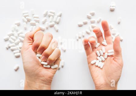 Palm hands full of white scattering pills. Woman gripes hand with capsules with medicines on light background. Flat lay, top view. Stock Photo