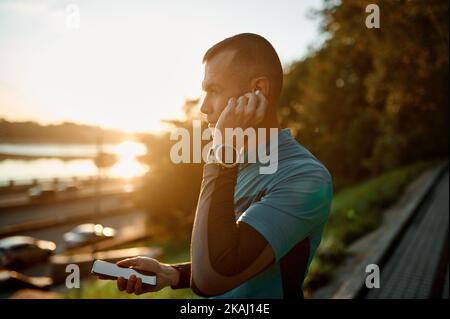 Sporty man using phone with earbuds jogging in park Stock Photo
