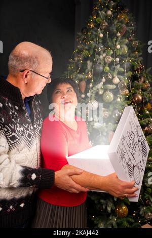 Man 60s giving a Christmas present to his woman. Opening gift box at christmas time. Christmas wonder concept Stock Photo