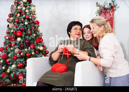 A cheerful 60 year old woman knitting a sock near the Christmas tree. Senio Stock Photo
