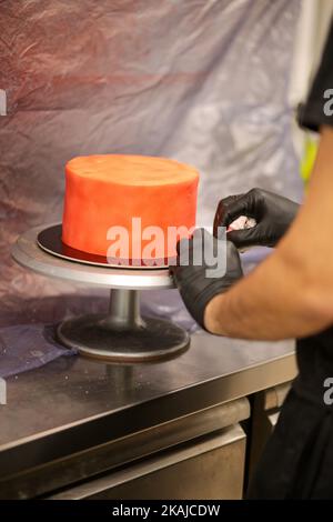 cook preparing a red frosted cake using air bush Stock Photo