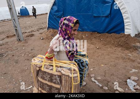 Photo taken in Qayyarah Jadah Camp near Qayyarah Jadah Camp on 23 December 2016. Girl carrying set of new blankets inside refugee camp. Two months into the military operation to retake the city from Islamic State of Iraq and the Levant (ISIL), The Mosul crisis continues to have a significant humanitarian impact. Humanitarian needs are severe among displaced families in and out of camps, vulnerable residents of newly- retaken communities, and people fleeing fighting in Mosul city.Current displacement has risen to 110,000 people. More than three quarters of displaced families are in camps and em Stock Photo