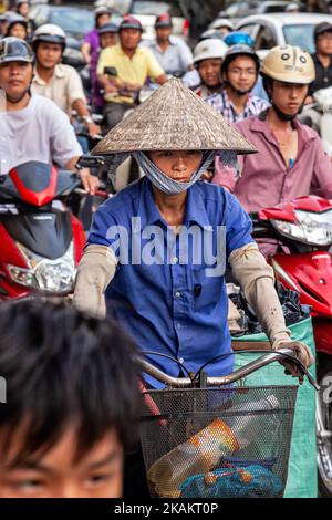 Vietnamese lady wearing bamboo hat on bicycle in motorcycle traffic jam, Ho Chi Minh City, Vietnam Stock Photo