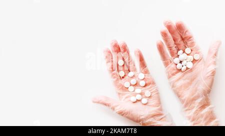 Doctor's palm hands in protective transparent gloves full of white scattering pills. Capsules with medicines on white background with copy space. Flat Stock Photo