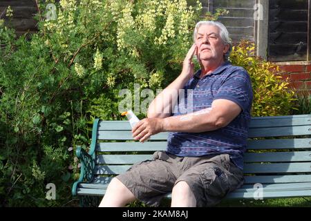 Senior or elderly man applying sun cream or blocker to his face. Sitting in the hot sun. Prevention from sunburn. Stock Photo
