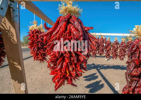 Bright red strings of chili peppers for sale on the side of the road in Tucson, Arizona. Set of hanging chili peppers outdoors against the blue sky. Stock Photo