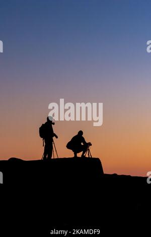 A vertical shot of the silhouettes of photographers taking pictures of sunrise Stock Photo