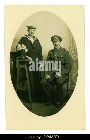 WW1 era postcard studio portrait of father and son looking solemn. The father is with the Middlesex Regiment (badge on cap) and the son is a naval cadet on HMS Impregnable, a training ship (HMS Impregnable on cap), Middlesex, S.E. England near London, circa 1916 Stock Photo