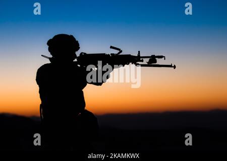 A shadow of a man in uniform holding a machine gun with sunset on a blurred background Stock Photo