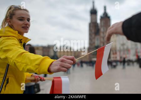 A young lady distibutes white and red flags on Poland's Flag Day. Flag Day was introduced to Poland in 2004, bridging the gap between International Workers' Day on 1st May and Constitution Day on 3rd May. Today, hundreds of different events were organise across the country, one of them, the 'White and Red relay RMF FM'. At 6 am, the relay carrying the Polish flag left Hel, in the North of Poland, with the flag arriving by boat in Sopot, and then from Gdansk to Warsaw by plane. In the capital, the main point of the program, was a relay of politicians. Another stop was Krakow, where the flag re Stock Photo