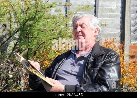 Elderly or senior man having trouble reading a book. Bad eyes and squinting. In need of spectacles. Stock Photo