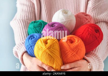 Female holding colorful or multicolored wool yarns on blue background. Many multi-colored balls of threads close-up. Needlework or knitting concept. Stock Photo