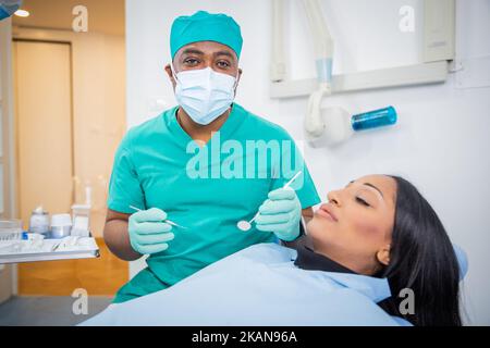 An African dentist is holding working tools in the dental office with his patient sitting. Stock Photo