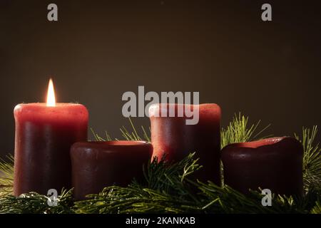 One red candle burning in an advent wreath  with evergreen boughs and red berries on a dark background with copy space Stock Photo