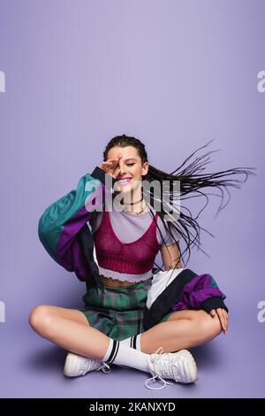 smiling woman in nineties attire sitting with crossed legs on wind on purple background,stock image Stock Photo