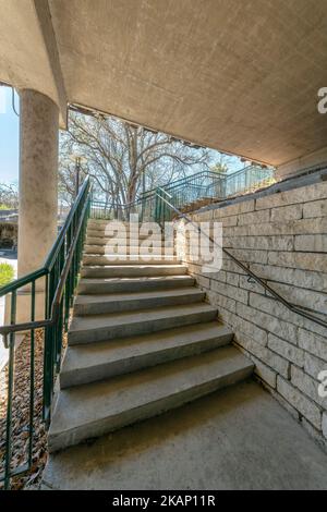 San Antonio, Texas- Staircase under a bridge with stone walls. Concrete steps of a stairs with metal handrails against the leafless tree background. Stock Photo