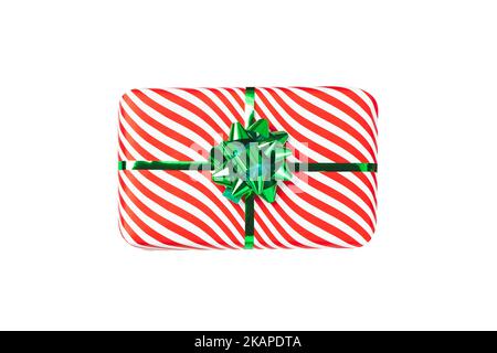 Wrapped red gift box with shiny green ribbon bow, object isolated on white background. A holiday striped wrapper, top view. Christmas present, new yea Stock Photo