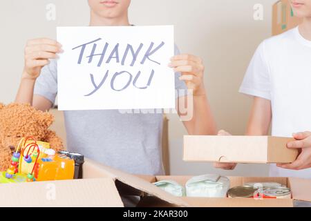 Thank you for donation. Volunteers collecting donations for charity. Teenagers holding paper sheet with message Thank you over cardboard boxes full of Stock Photo