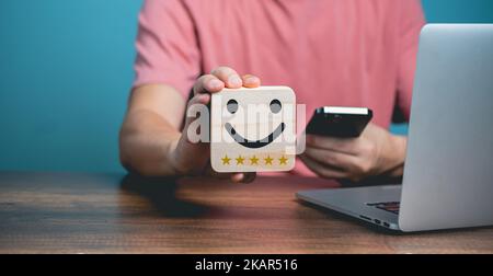 Customer service satisfaction concept, Young businessman using Mobile Phone and holding happy face wooden  with smiling face, satisfaction five stars Stock Photo