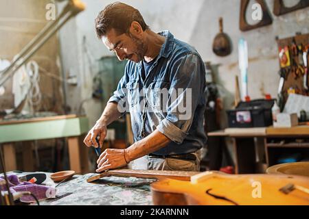 A luthier adjusts the truss rod of a semi-acoustic guitar in his service workshop - technician setting up the guitar neck - craftsman people lifestyle Stock Photo