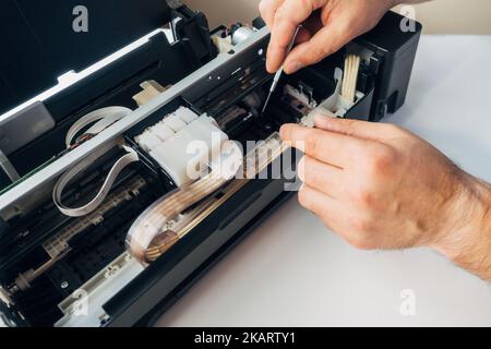Maintenance and repair of printers. Master's hands with screwdriver. Background. Urgent repair of office equipment at home or in office.. Stock Photo