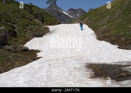 An elderly man with two trekking poles and a backpack is walking uphill on the snow. Stock Photo