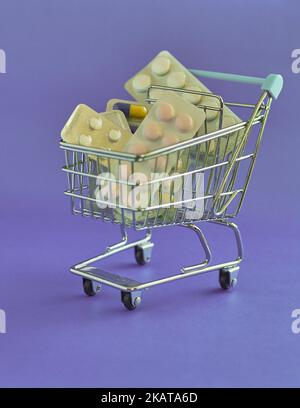 A vertical shot of a mini shopping cart with pills isolated on a purple background Stock Photo