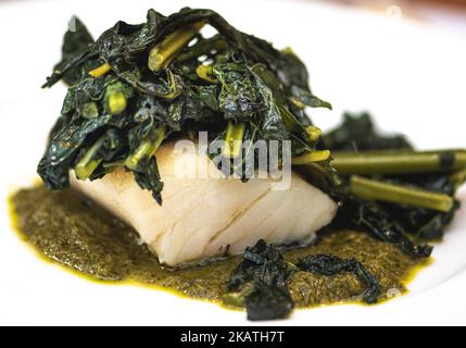 Steamed cod fillet with leaves and black cabbage sauce just served in a white plate, close up Stock Photo