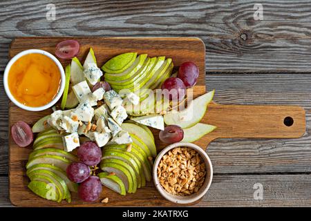 Sliced Blue cheese, dor blue or roquefort and fruits (grapes, pears), nuts and honey on a board. Exquisite appetizer for wine. Fruity cheese plate. Stock Photo