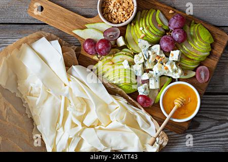 Ingredients for making a phyllo dough tart, fruits (grapes, pears), cheese and nuts with honey. Cooking mediterranean cuisine. Stock Photo