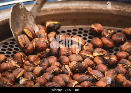 Roasting chestnuts in a bowl or grill on an open fire in a street food market, close up Stock Photo