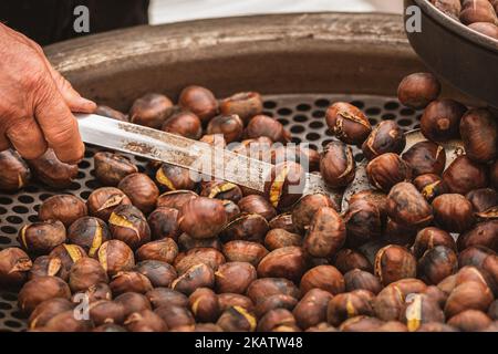 Roasting chestnuts in a bowl or grill on an open fire in a street food market, close up Stock Photo