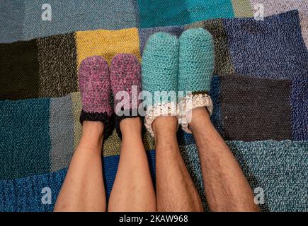 Feet of man and a woman wearing warm handmade slippers made of wool, staying warm in the winter Stock Photo