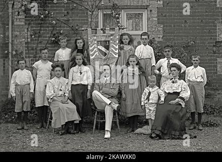 A group photograph of pupils and two teachers at Mileham Elementary (Primary) School, Breckland, Norfolk, England, UK c. 1908. The boys and girls wear an interesting mix of clothing. Some are very smartly dressed – as are their teachers. Some of the boys seem dressed for sporting activity. They are posed with a banner with the school shield on it. It also indicates winners of their school competition (‘challenge trophy’) – it seems that Scarning class often won the award! The school founded in 1677, but it closed in 2015, like many rural communities – a vintage Victorian/Edwardian photograph. Stock Photo