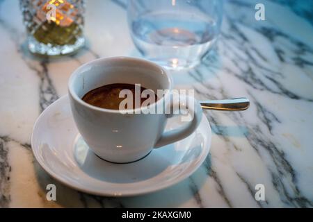 Close up espresso coffee in cup with a glass of water and a background and a tea light twinkling on a marble table. Stock Photo